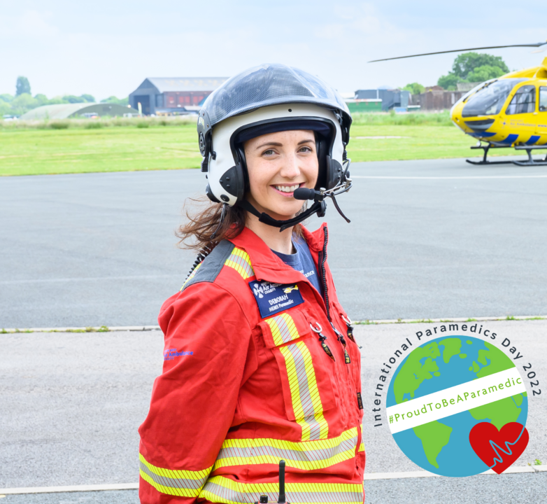 Image of Critical Care Paramedic Deborah by the NWAA helicopter in her red flight suit and helmet