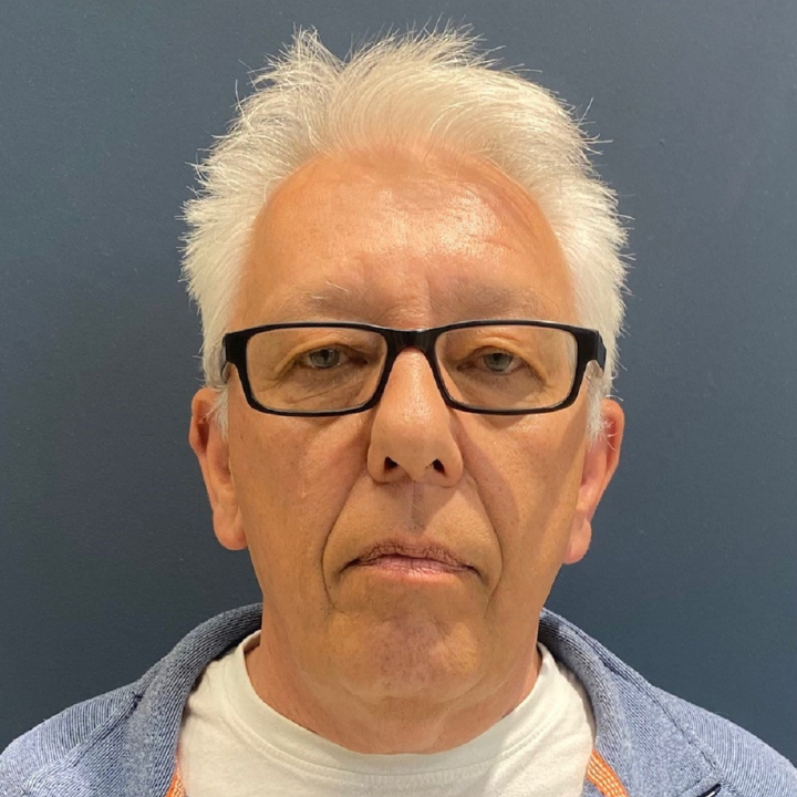 Image of lottery canvasser Andrew Dean. he has short white hair, black rectangle glasses and a blue jumper over a white shirt.