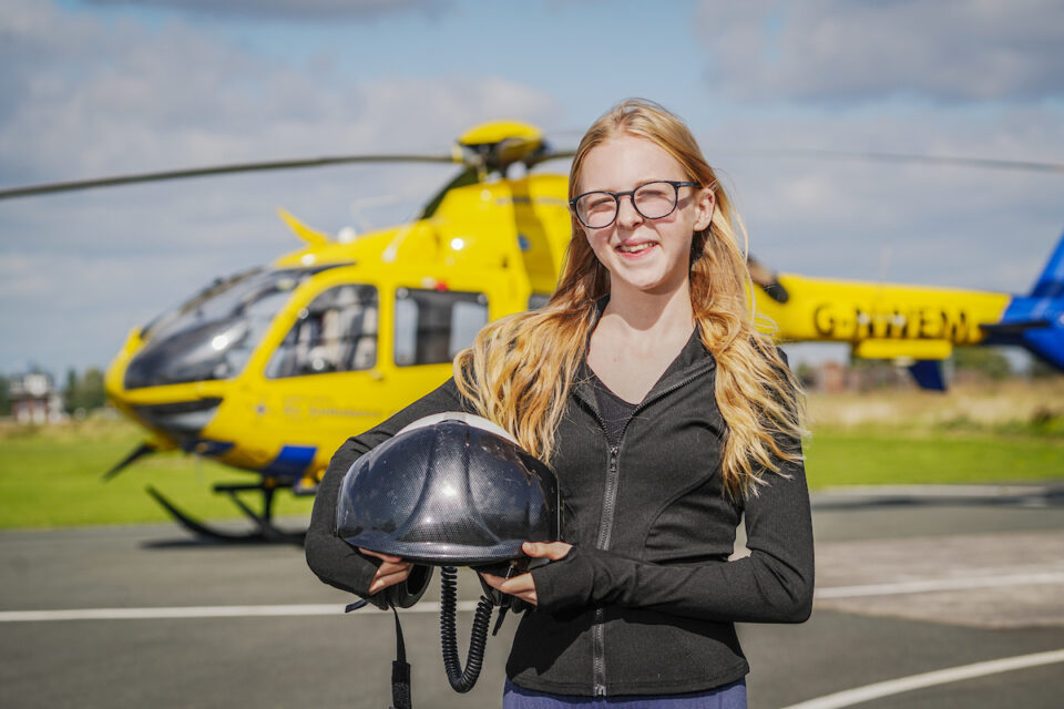 Ruby holding helmet of air ambulance crew, stood in front of one of the charity's helicopters