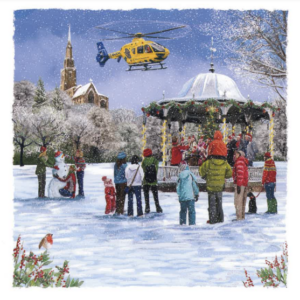 A bandstand in the middle of a snowy park is surrounded by people in winter jackets watching a North West Air Ambulance helicopter going past.