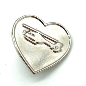 A silver metal heart pin bade with a debossed North West Air Ambulance helicopter in the centre.