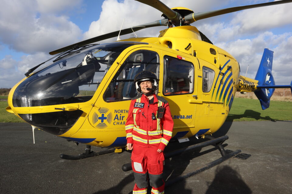 Critical care paramedic in red flight suit stood in front of the helicopter