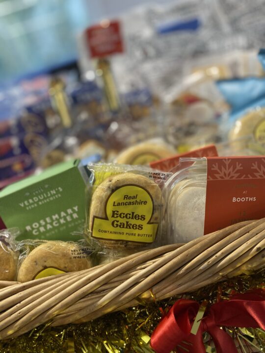 Christmas hamper sat on a table filled with foodie treats like mince pies, gingerbread and Eccles cakes. 