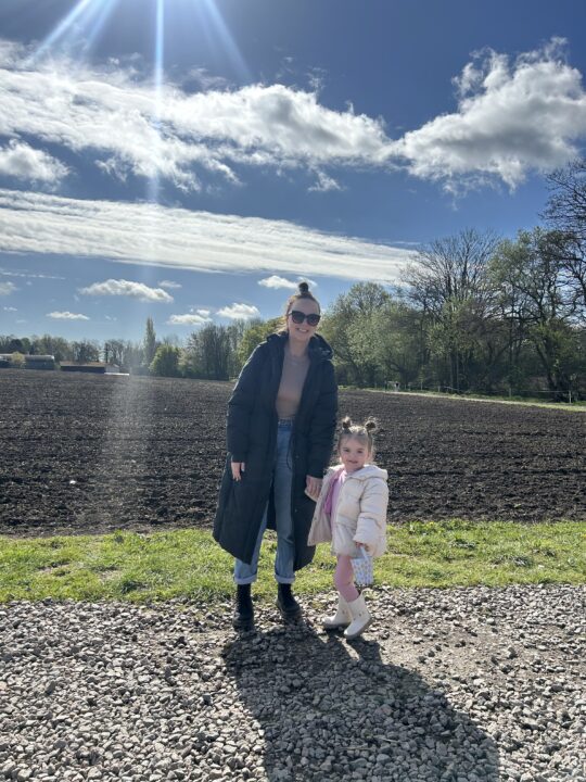 Bethany and her Daughter stood holding hands in front of a field