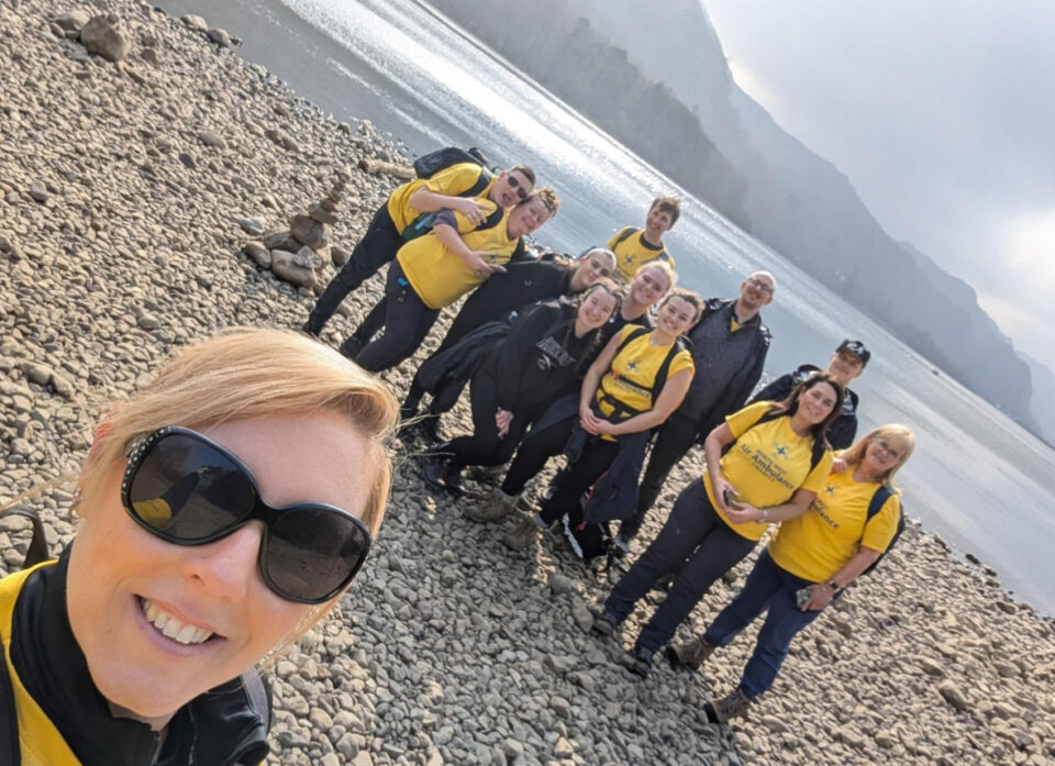 Blonde lady taking a selfie with the M&S fundraisers stood in the background wearing branded yellow T shirts