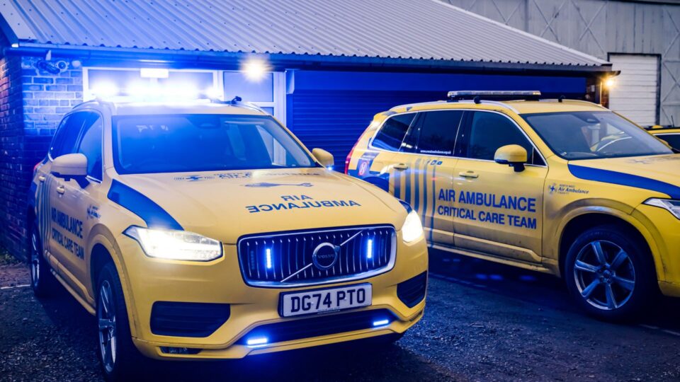Two yellow North West Air Ambulance Charity critical care response vehicles parked outside a building at night, with blue emergency lights illuminated.
